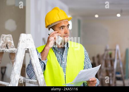 Young foreman with documents in his hands is talking on a mobile phone Stock Photo