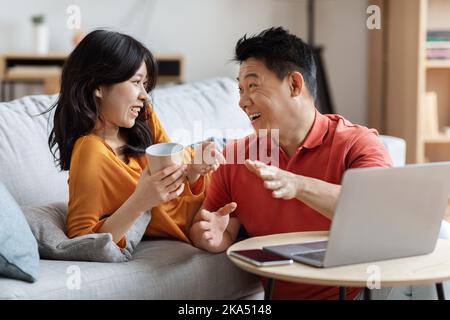 Portrait of cheerful korean spouses using laptop together, having conversation Stock Photo
