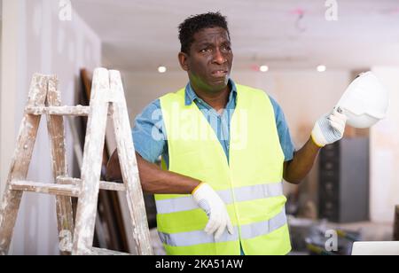 Portrait of disgruntled african american worker in yellow vest in cottage under construction Stock Photo