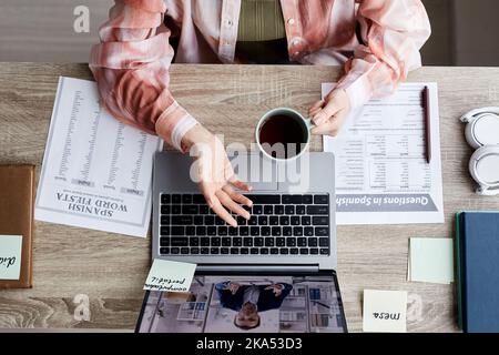 Above angle of young woman with cup of coffee communicating with tutor on laptop screen during online lesson of Spanish language Stock Photo
