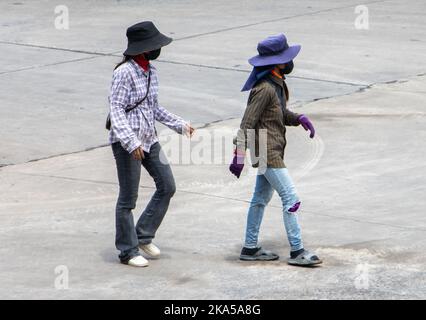 Two construction female workers with hidden faces are walking down a sunny street, Thailand Stock Photo