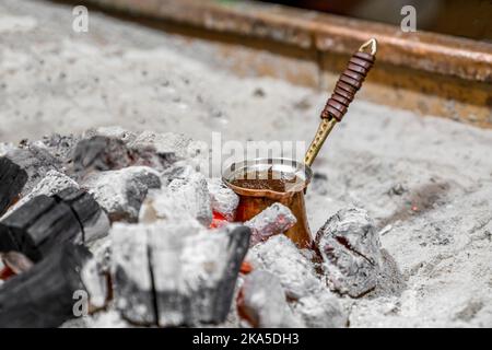 Natural ground coffee is brewed in copper turk on coals according to Turkish tradition. Close-up Stock Photo