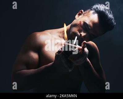 Dark, flame and man lighting a cigarette with a lighter to smoke after a fight in a studio. Young, dangerous and smoker or fighter from Puerto Rico Stock Photo