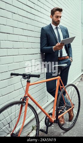 The urban landscape is his domain. a handsome young businessman using a digital tablet while standing alongside his bike outdoors. Stock Photo