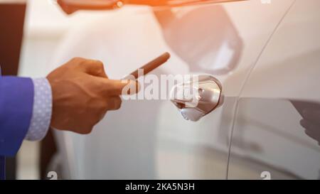 Black salesman opens car using app on mobile phone Stock Photo