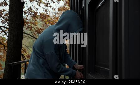 Thief in dark clothes picks door lock and enters house Stock Photo