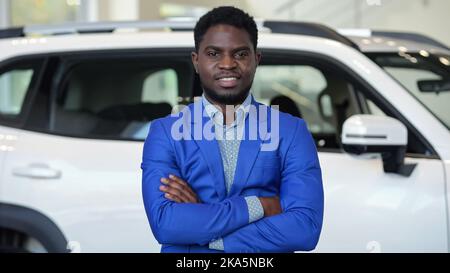 Smiling African American man stands against car in salon Stock Photo
