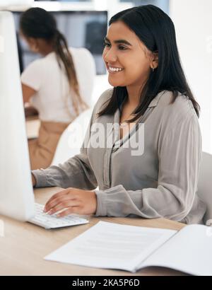 Computer, report and typing with an indian woman in business working on a desktop in her office at work. Internet, email and desktop with a young Stock Photo