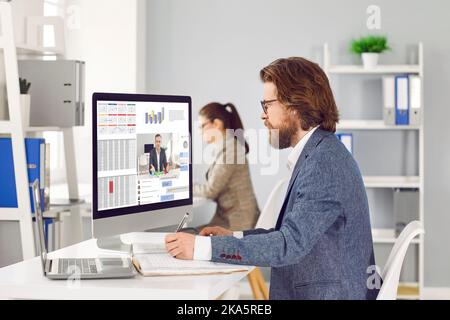 Employees sitting at office desks, working on computers and using business software Stock Photo