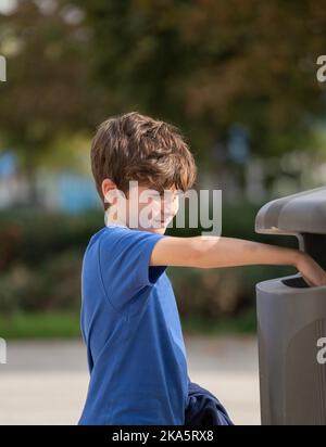 Caucasian kid 9 year old try to throw trash in public trashcan. Concept of garbage, Recycle environment, save world. Stock Photo