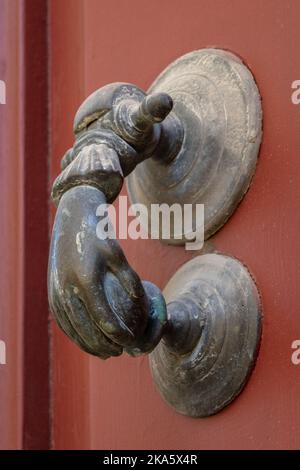 Closeup view of beautiful vintage brass door knocker in shape of hand holding ball isolated on ancient orange red wooden door, Montpellier, France Stock Photo