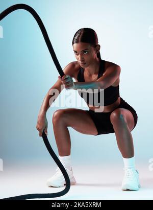 Battle rope, exercise and fitness model in a studio with energy, motivation and training. Healthy, strong and slim woman athlete from India doing a Stock Photo