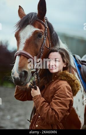 Who could feel down when its time to saddle up. a teenage girl standing next to her pony on a farm. Stock Photo