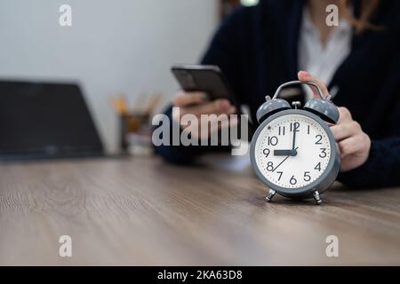 Alarm clock on wooden table with business working at home. Time concept at early morning or overtime in evening Stock Photo