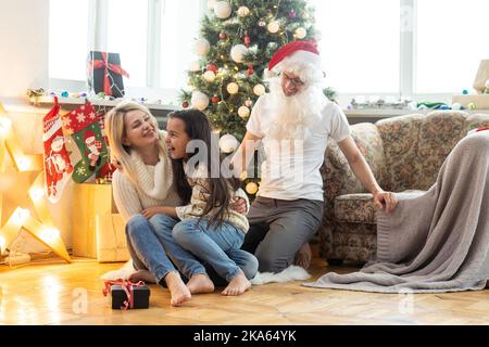 Portrait of happy family with kid holding festive party props for photo booth. Mother in Santa hat, father, child in sweater having fun on Christmas Stock Photo