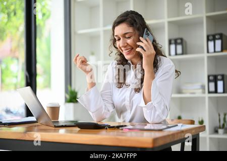 Beautiful millennial caucasian businesswoman or female boss having a phone call with someone while working in her office. Stock Photo