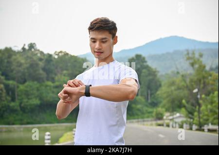 Close-up, Handsome and healthy young Asian man in sportswear checking his heart rate and calories burned from running on his smart watch. Activity and Stock Photo