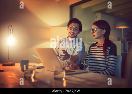 Just a few tweaks to this and well be done. two young designers working late on a laptop in an office. Stock Photo