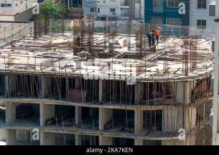 chinese and black african workers on the top of the roof of a construction site building occupied with ferroconcrete in a sunny day. Stock Photo