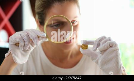 Female hand holding magnifying glass and looking through at golden coin Stock Photo