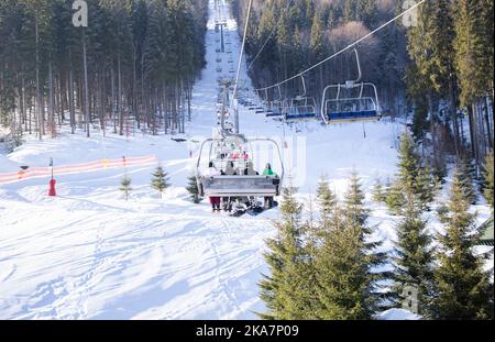 chair lift carrying unrecognizable skiers to top of the snow-covered slope of the Carpathian mountains. cold winter sunny day, outdoor activities. Ski Stock Photo