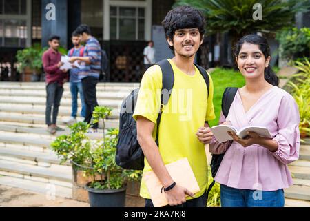 happy smiliung students looking at camera while preparing for exams by reading books at college campus - concept of knowledge, education and Stock Photo