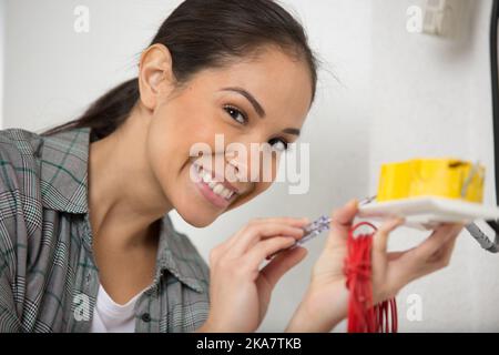 happy female electrician fixing electric cables in socket Stock Photo