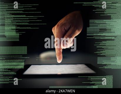 Touching his way to software programming. an unrecognizable man cracking a code using a tablet in the dark. Stock Photo