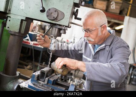 senior metal worker using industrial drilling machine in workshop Stock Photo