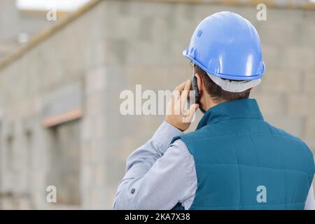 male builder foreman on building site using phone and plans Stock Photo
