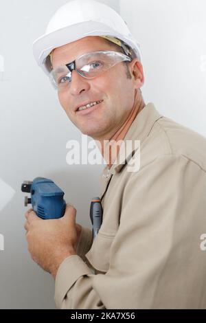 mature builder using drill on wall Stock Photo