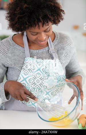 woman beating eggs at home with wire whisk in bowl Stock Photo