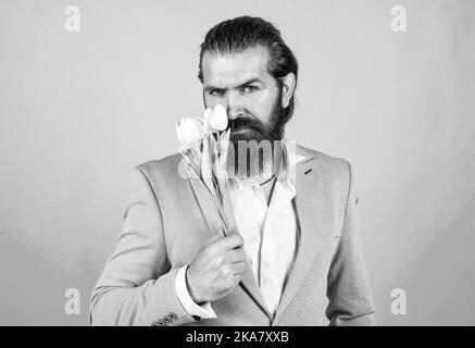 smelling good. brutal handsome man with gift. valentines or womens day. masculinity and charisma. formal party dress code. bearded hipster hold tulip Stock Photo