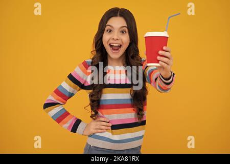Teenager child with coffee cup isolated on yellow studio background. Girl drinking take away beverage. Amazed teenager. Excited teen girl. Stock Photo