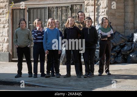 During yeshiva recess, 8 orthodox Jewish boys, each with long peyot, stare at something across the street. In Brooklyn, New York City. Stock Photo