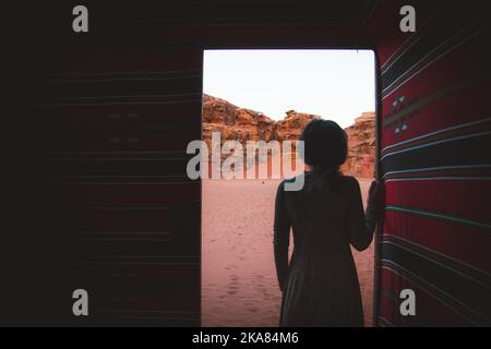 Woman person stand in desert bedouin camp inside traditional tent with open door enjoy wadi rum desert cliffs and textures early morning