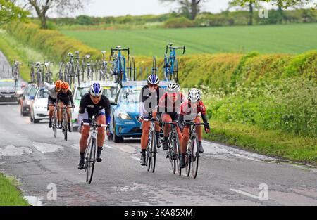 Racing cyclists with support vehicles with cycles on their roofs following close behind. Stock Photo