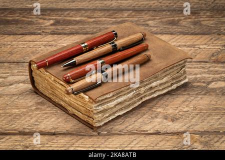 retro leather-bound journal with decked edge handmade paper pages and a collection of stylish pens on a rustic wooden table, writing and journaling co Stock Photo