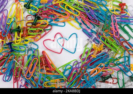 A blue and red paper clip in the shape of a heart in the middle of many ordinary paper clips. Two unique hearts in an ordinary world. Stock Photo