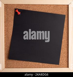Cork note board with wooden frame with blank black square sheet for writing text hanging on buttonpin. Notice board with empty reminder note. Copy spa Stock Photo