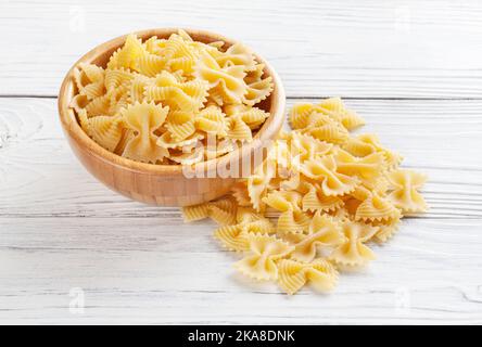 Uncooked farfalle rigate pasta in wooden bowl on white wooden background Stock Photo