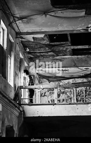 A vertical grayscale shot of a man looking out the windows of an abandoned psychiatric department building in Owinska, Poland Stock Photo