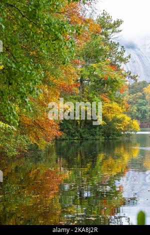 Vibrant autumn color reflecting in a still lake with the mist covered granite of Stone Mountain in the background at Stone Mountain Park in Atlanta. Stock Photo