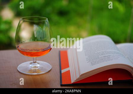 Whiskey in snifter glass and book outdoor with on wooden table Stock Photo