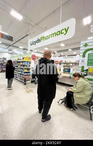 People wait at Lloyds Pharmacy inside Sainsburys, Wandsworth, London. October 2022. - EDITOR NOTE - Faces blurred. Stock Photo