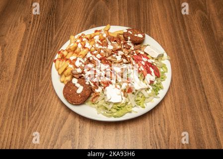 Kebab menu plate with big heap of chicken and lamb meat with salad and french fries, falafel, white onion and fresh cheese and drizzled with lots of s Stock Photo
