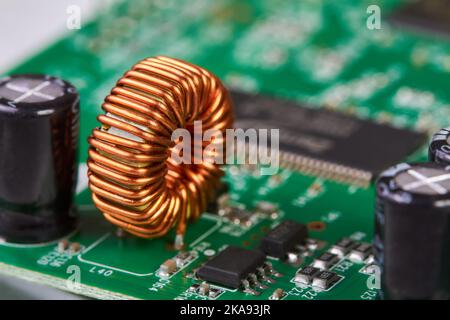 Orange inductor with copper wire on green printed circuit board detail Stock Photo