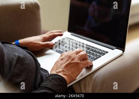 man working with his laptop on his legs, detail cropped on hands typing on keyboard - technology concept of business remote working and freelance acti Stock Photo