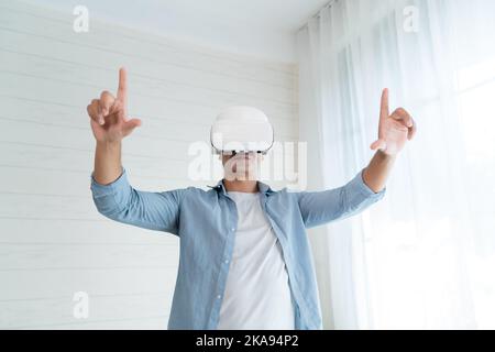 A happy man in a VR headset with open hands enjoying a virtual reality experience in a white bedroom Stock Photo
