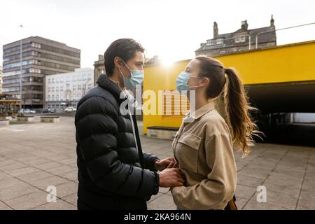 A young couple spending the day in Newcastle Upon Tyne. They are standing on a paved area in the city centre while looking at each other and holding h Stock Photo